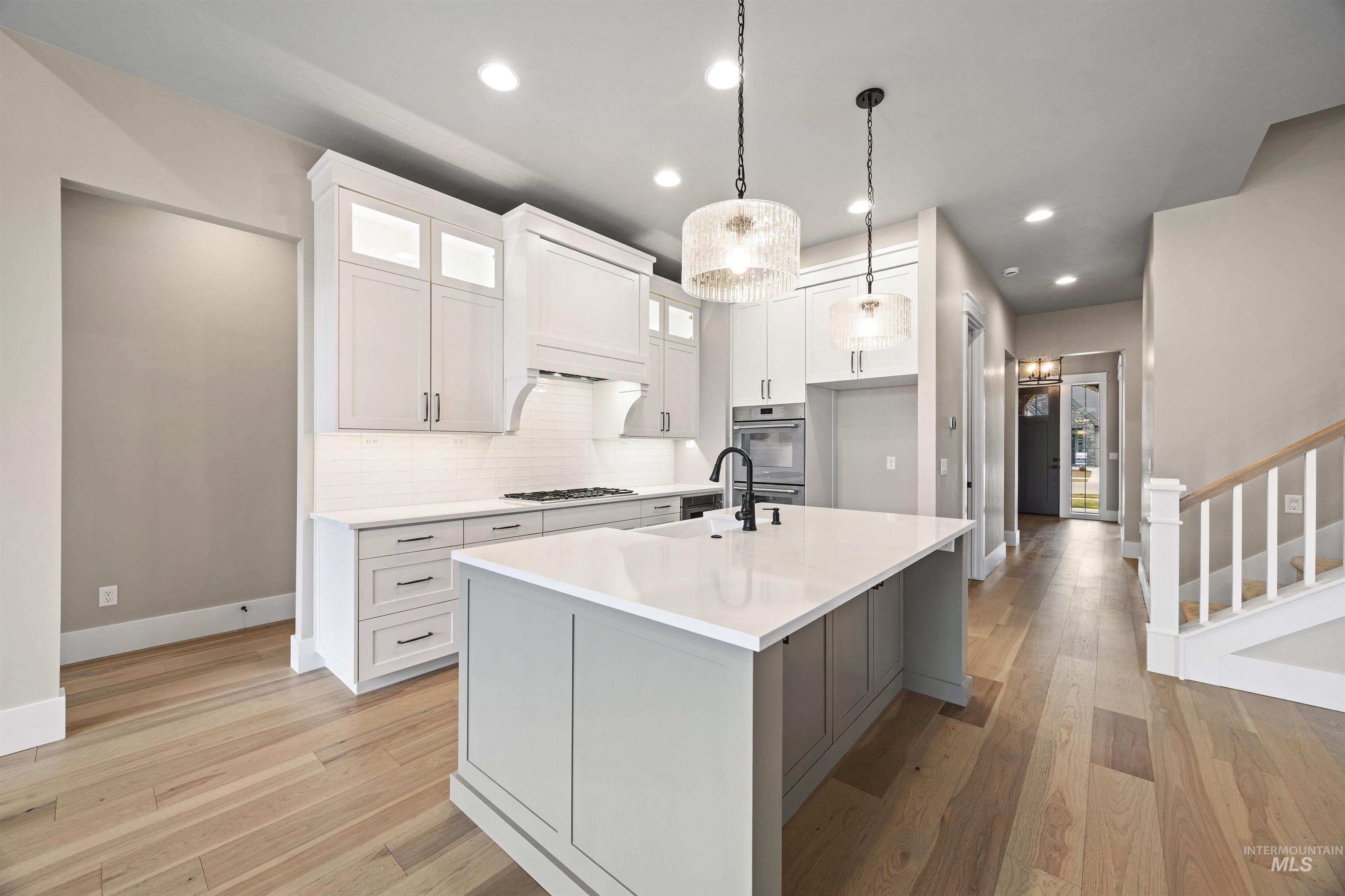 934 East Escalation Street Meridian, ID 83642 - Photo 28 of 50 Two tone kitchen with glass fronted cabinets, light wood-style flooring, a center island with sink, hanging light fixtures, and tasteful backsplash