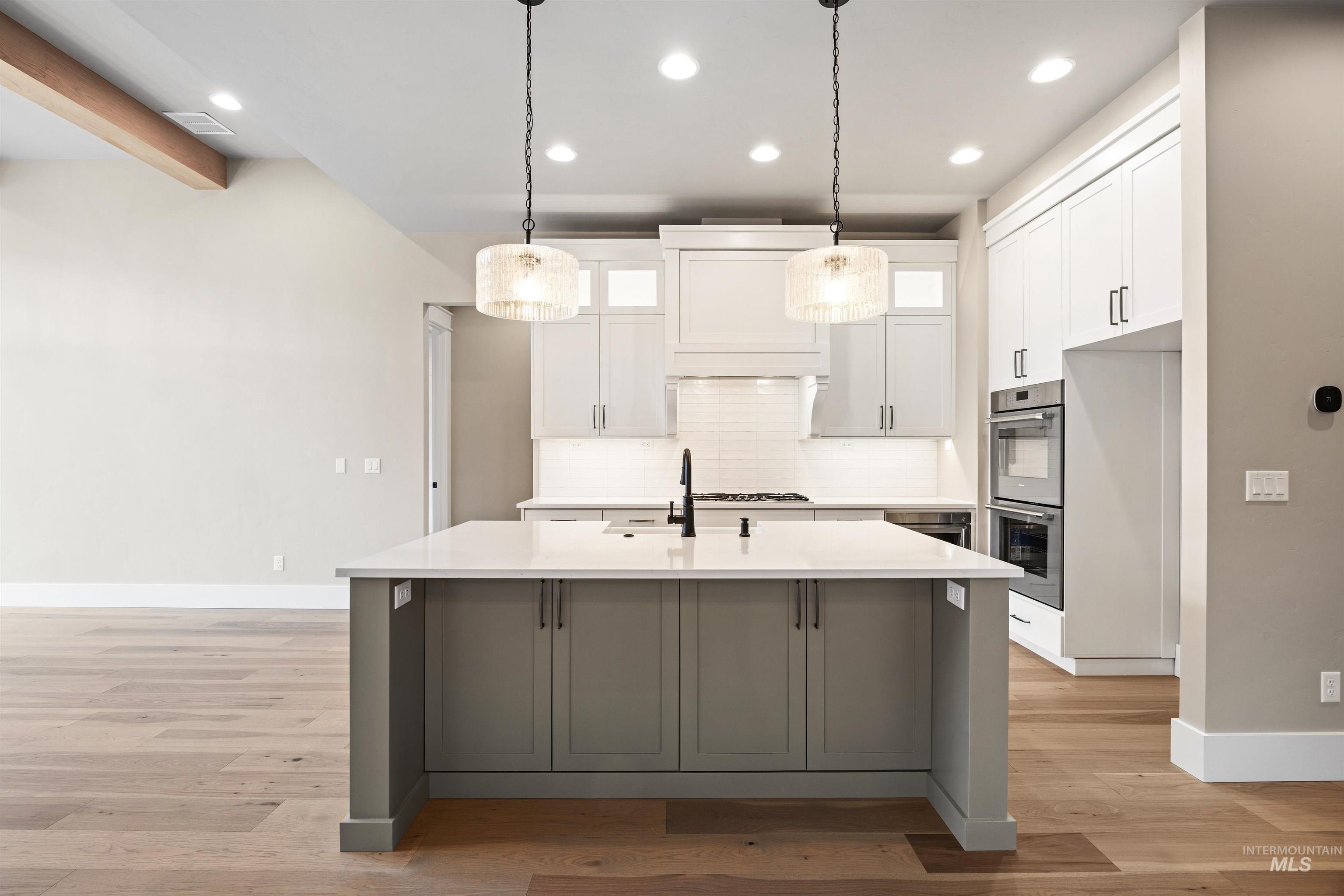 934 East Escalation Street Meridian, ID 83642 - Photo 29 of 50 Two tone kitchen with dual tone cabinetry, a center island with sink, light wood-style floors, decorative backsplash, and stainless steel appliances
