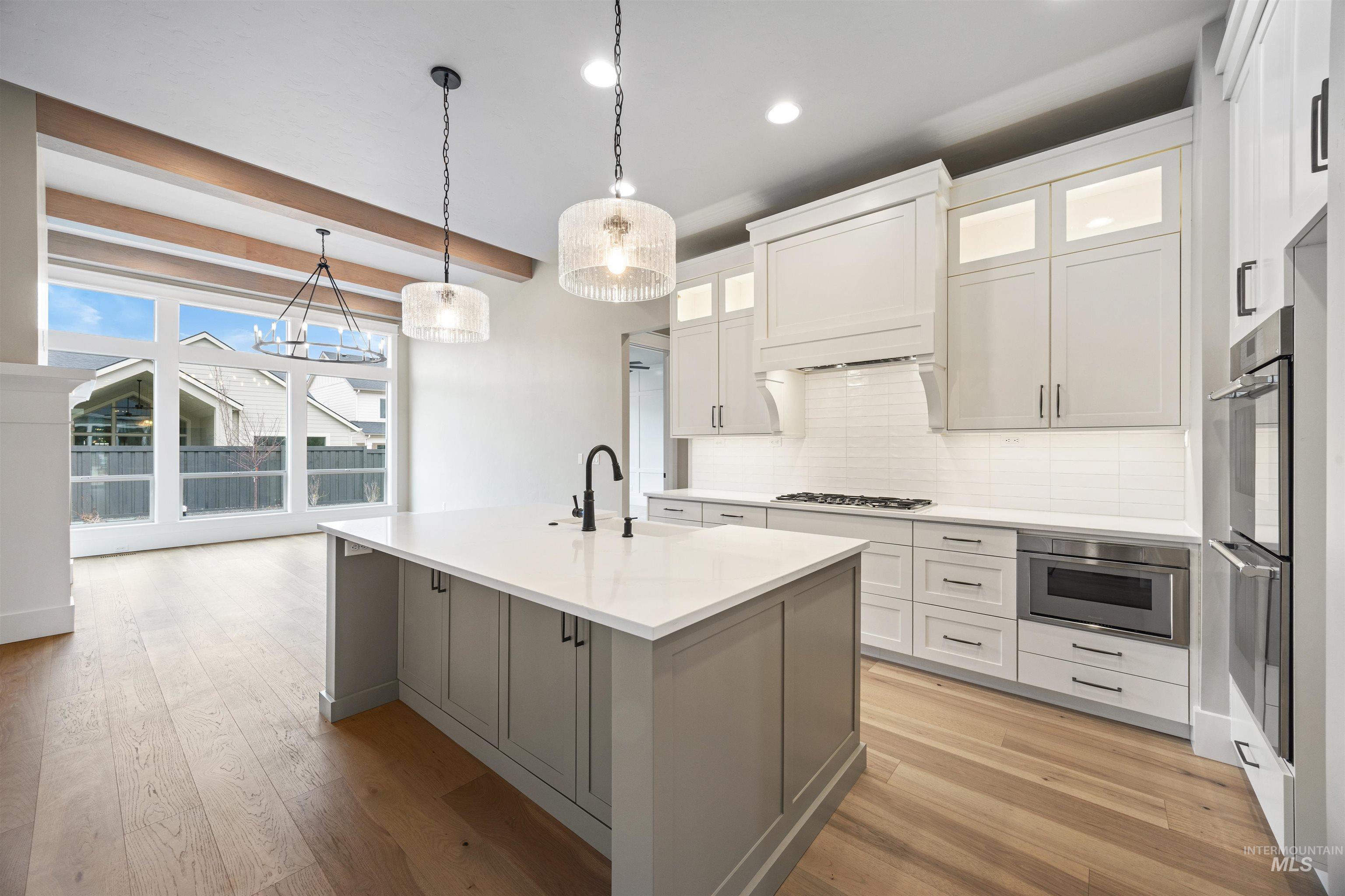 934 East Escalation Street Meridian, ID 83642 - Photo 31 of 50 Dual tone kitchen with decorative light fixtures, a center island with sink, decorative backsplash, light wood-style flooring, and two tone color scheme