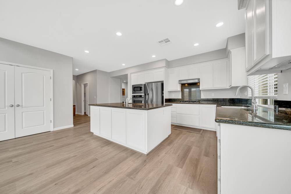 20300 Panoz Road Patterson, CA 95363 - Photo 13 of 61 a large kitchen with stainless steel appliances granite countertop a large counter top and a stove top oven with wooden floor