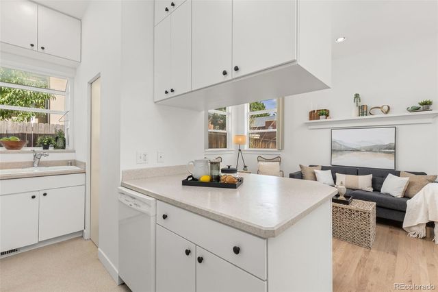 a kitchen with a sink dishwasher and white cabinets with wooden floor