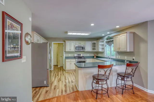 a kitchen with stainless steel appliances granite countertop a refrigerator a sink dishwasher a stove and white countertops with wooden floor