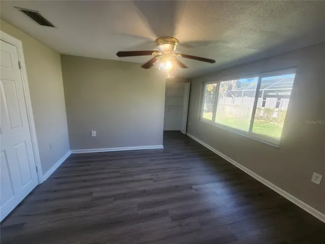 an empty room with wooden floor fan and windows