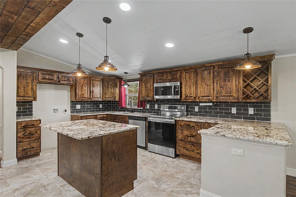 1701 Central Road Weatherford, TX 76088 - Photo 5 of 40 Kitchen with stainless steel appliances, light granite counters, a center island, decorative subway tiled backsplash, shiplap ceiling with recessed and pendant lighting and ornamental molding.