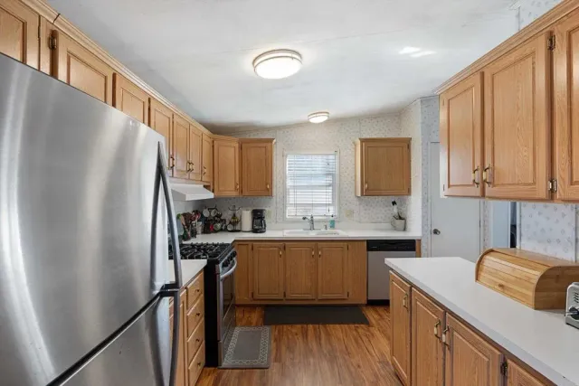 a kitchen with stainless steel appliances granite countertop a refrigerator a sink dishwasher a stove and white countertops with wooden floor