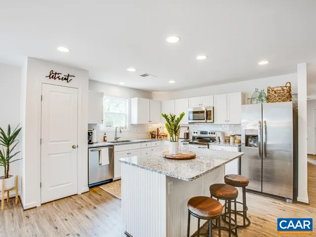 a kitchen with stainless steel appliances granite countertop a refrigerator a stove a sink a dining table and chairs with wooden floor