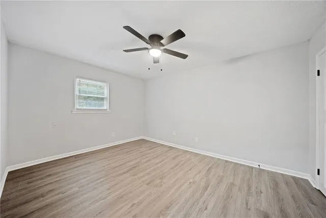 an empty room with wooden floor ceiling fan and windows