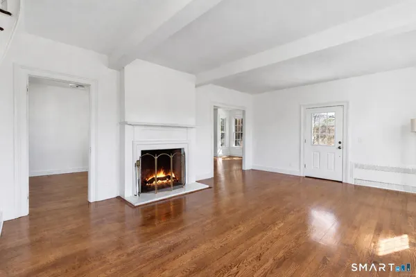 a view of an empty room with wooden floor fireplace and a window