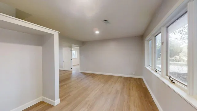 a view of an empty room with wooden floor and a window