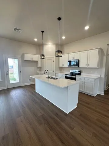 a kitchen with kitchen island wooden floors white cabinets appliances and a sink