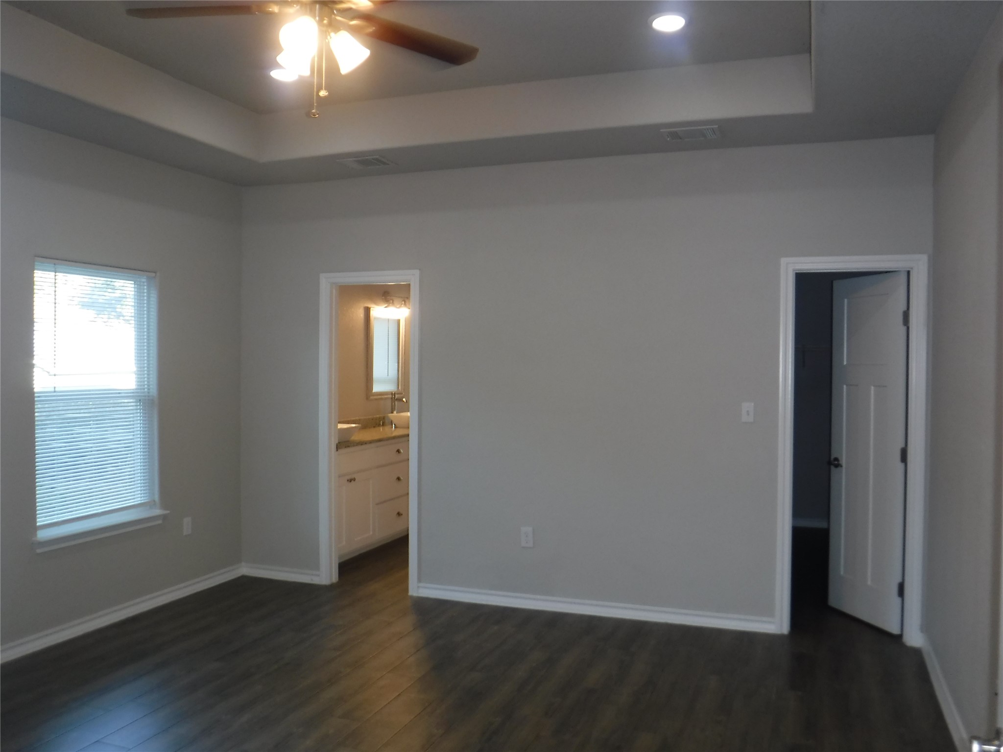 1633 Cree Trail Kingsland, TX 78639 - Photo 5 of 11 Unfurnished bedroom with a tray ceiling, dark wood-style floors, ensuite bathroom, and a ceiling fan