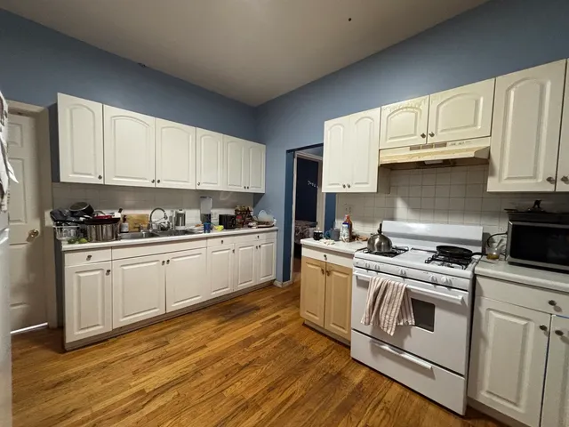 a white kitchen with wooden floors and stainless steel appliances