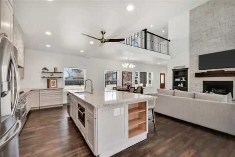 a large white kitchen with kitchen island a stove a sink a refrigerator and white cabinets with wooden floor