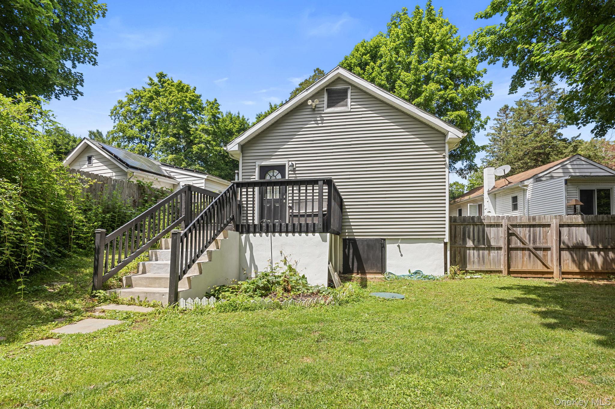 10 Batavia Road Patterson, NY 12563 - Photo 29 of 42 Rear exterior featuring horizontal siding, a private wood deck with dark railings, and a concrete staircase leading to a ground-level patio.