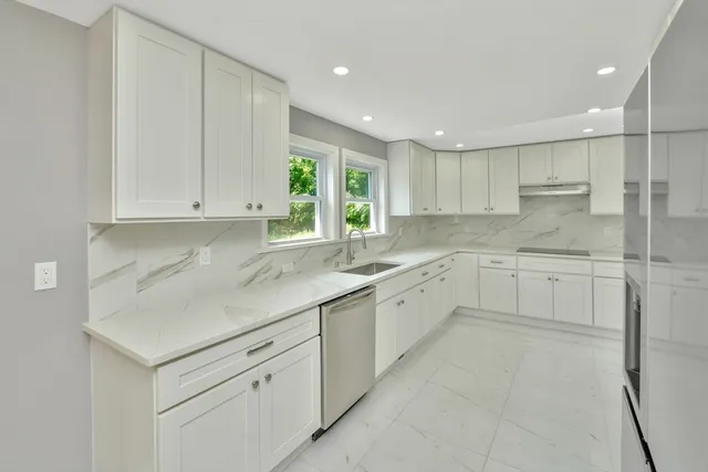 a kitchen with white cabinets appliances a sink and a window
