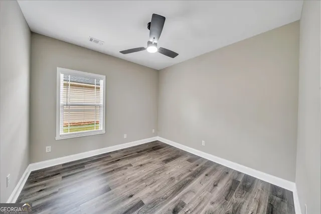 an empty room with wooden floor chandelier fan and windows