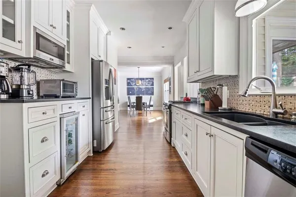 a kitchen with stainless steel appliances kitchen island granite countertop a stove a sink dishwasher and white cabinets with wooden floor