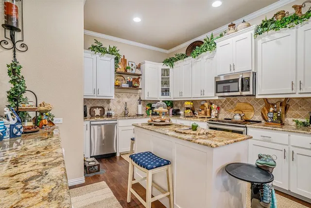 a kitchen with stainless steel appliances granite countertop a stove a sink dishwasher and white cabinets with wooden floor