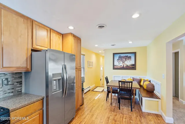 a kitchen with stainless steel appliances granite countertop a refrigerator a stove a sink a dining table and chairs with wooden floor