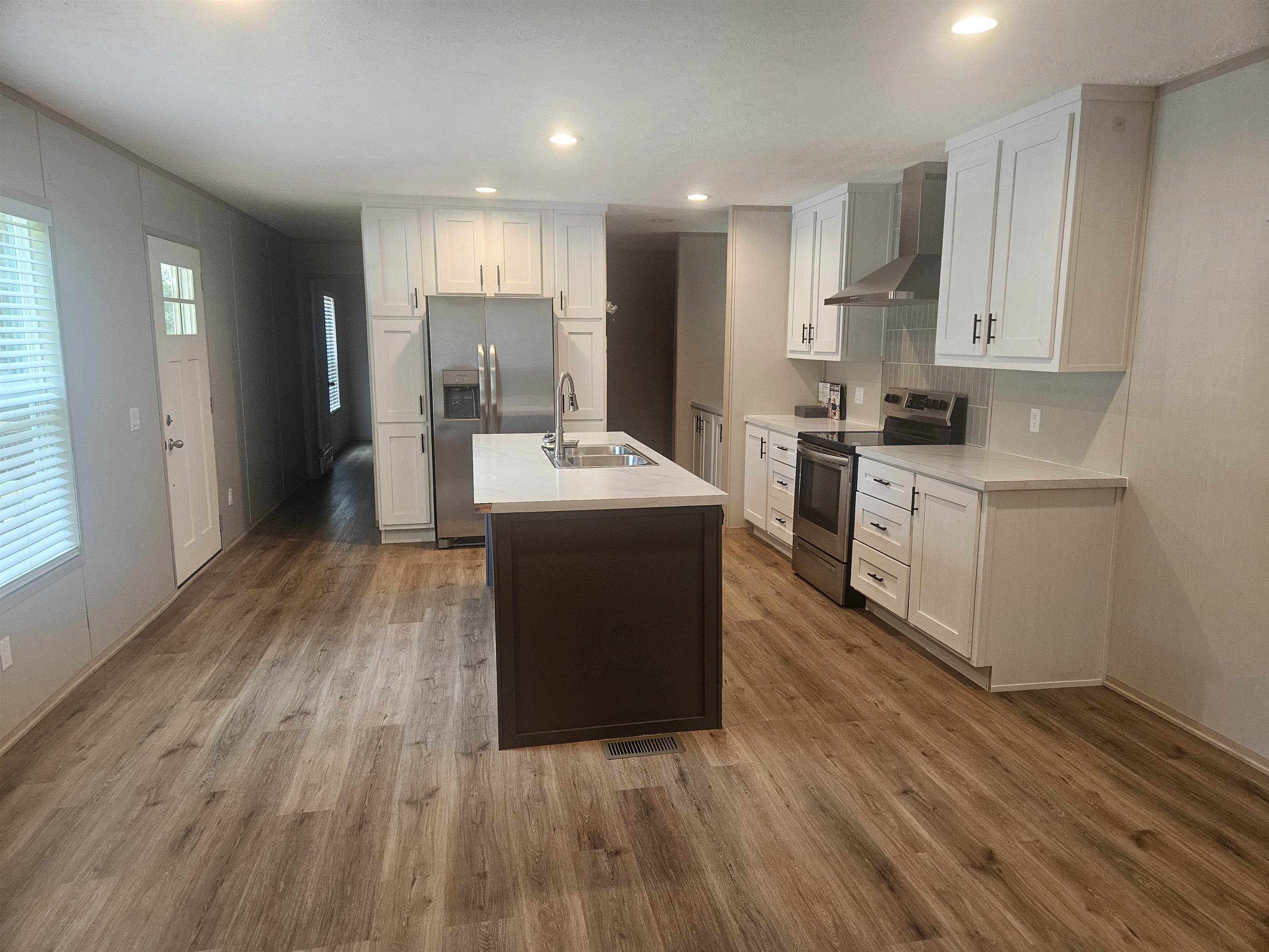 75 Pittman Road, Unit ROAD Somerville, TN 38068 - Photo 3 of 26 Spacious kitchen featuring an island with an integrated sink, stainless steel appliances, white cabinetry, light-toned countertops, and wood-finish flooring