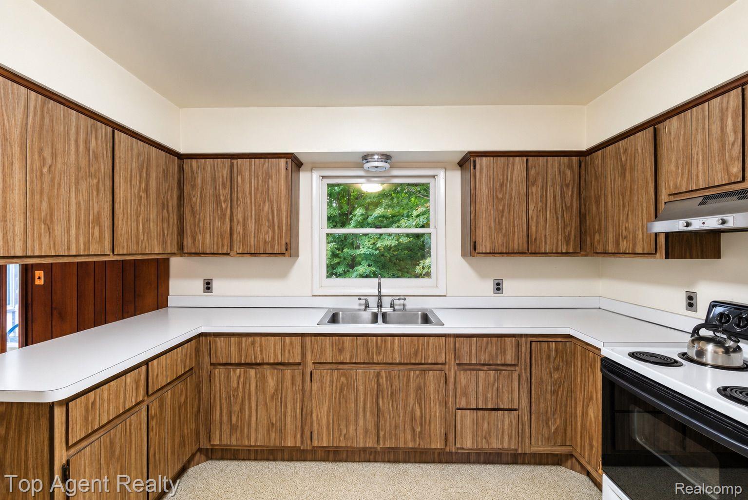 8269 Currie Road Northville, MI 48168 - Photo 5 of 80 U-shaped kitchen layout with wood-finish cabinetry, white countertops, a double basin stainless steel sink, and a built-in range hood