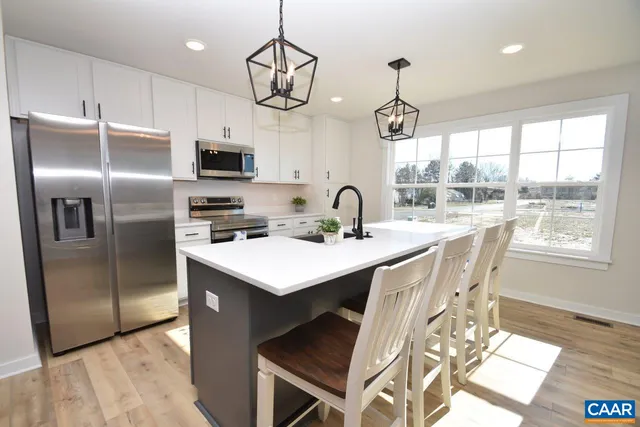 a kitchen with stainless steel appliances granite countertop a sink a stove a refrigerator cabinets and a dining table with wooden floor