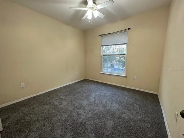 an empty room with chandelier fan and windows