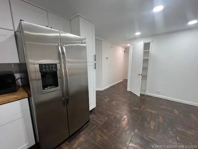 a view of a refrigerator in kitchen and an empty room with wooden floor