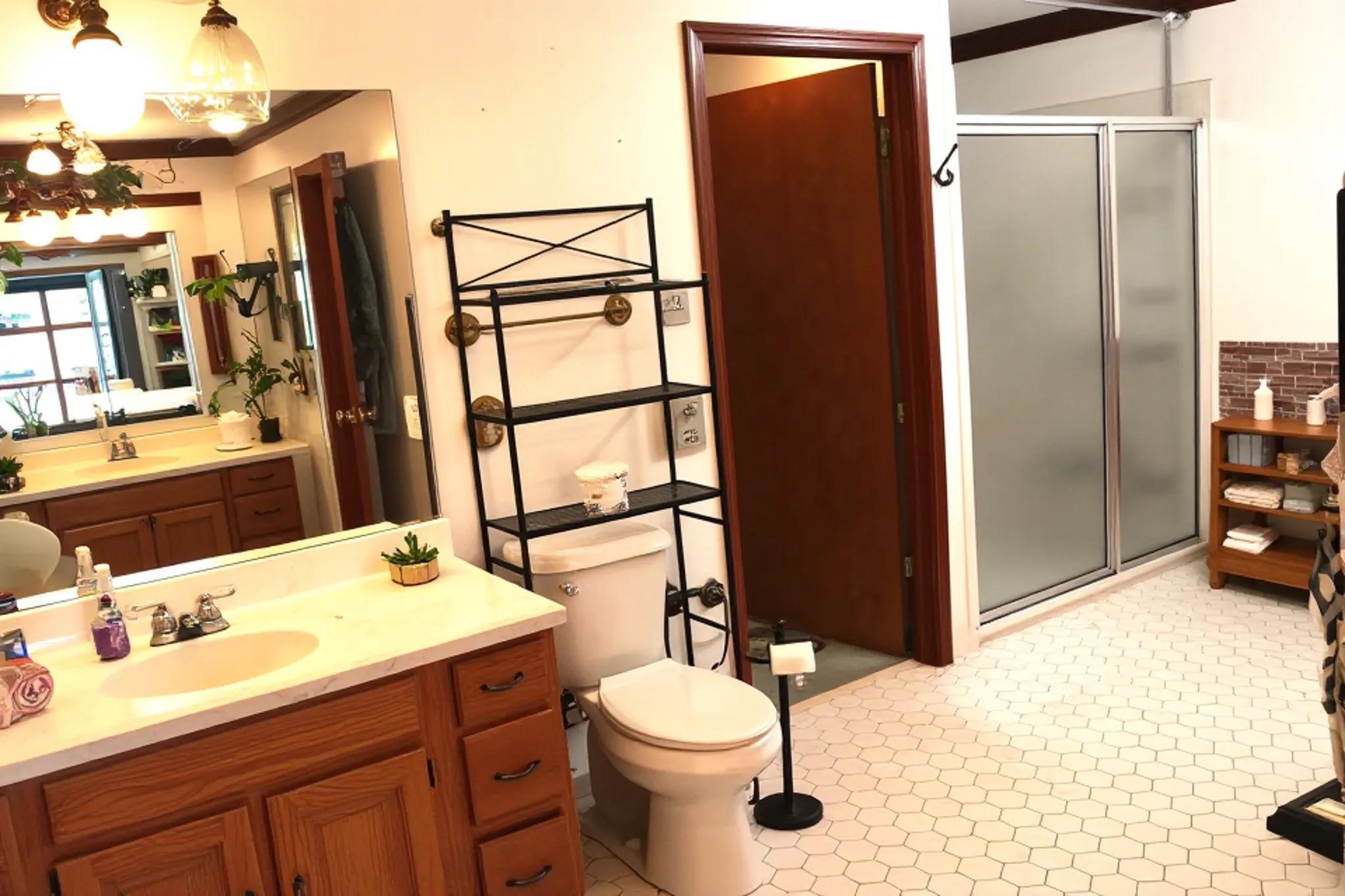 937 Kelleys Chapel Road Burlison, TN 38015 - Photo 16 of 40 Bathroom featuring hexagonal tile flooring, a dual vanity with oak-finish cabinetry, a shower with frosted glass doors, and a decorative brick-style wall accent