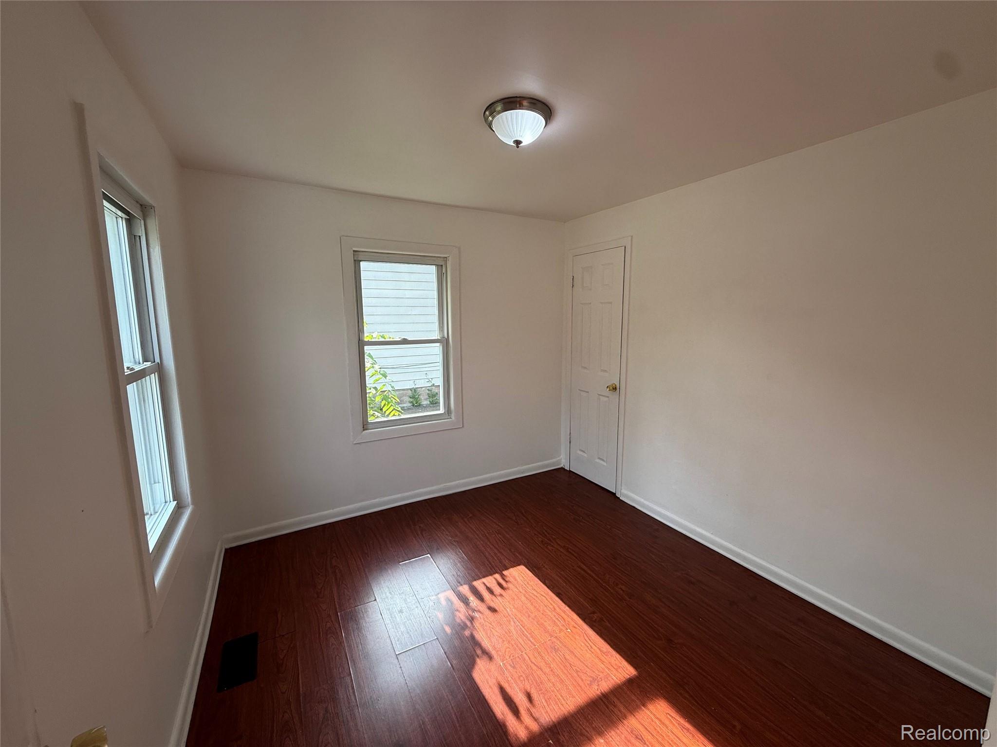 2194 East Bristol Road Burton, MI 48529 - Photo 8 of 13 Interior room featuring wood-finish flooring, two windows with white trim, and a ceiling-mounted light fixture