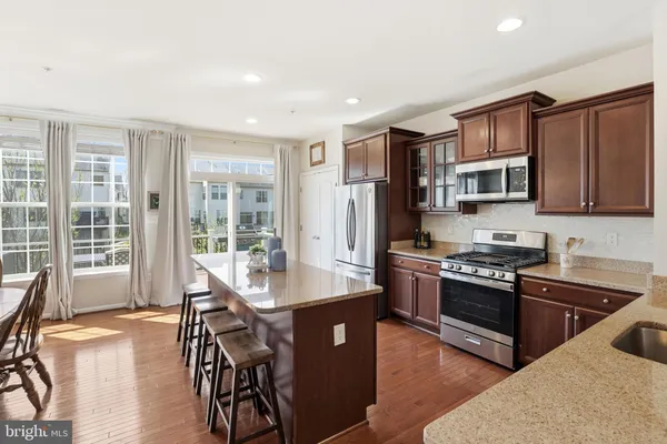 a kitchen with stainless steel appliances granite countertop a stove a refrigerator a sink a dining table and chairs with wooden floor