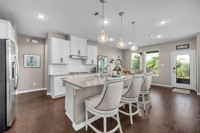 a kitchen with stainless steel appliances kitchen island granite countertop a dining table chairs and white cabinets