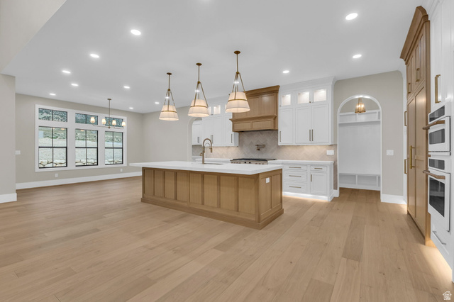 2828 Jojo Road Eagle Mountain, UT 84005 - Photo 11 of 63 Open-concept kitchen featuring a large central island with a solid surface countertop, light wood-finish flooring, two-tone cabinetry, and integrated double ovens