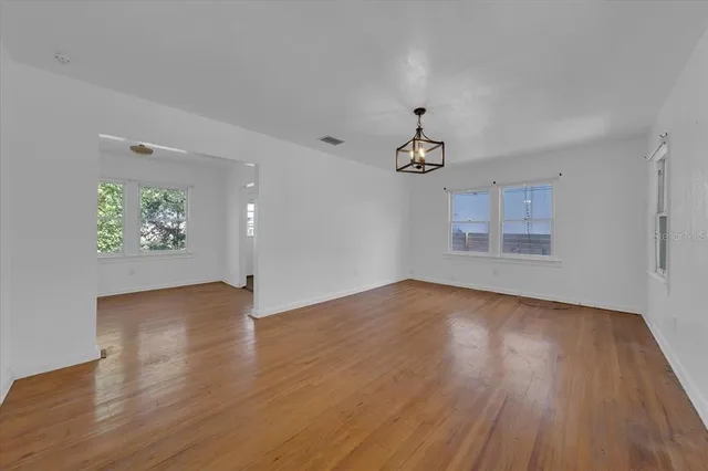 an empty room with wooden floor chandelier and windows