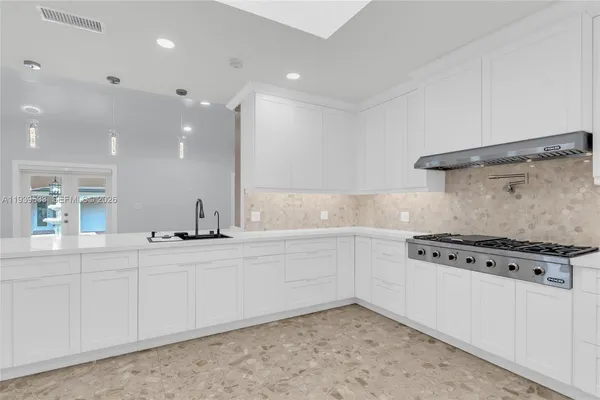 a large white kitchen with kitchen island a stove a sink a refrigerator and white cabinets