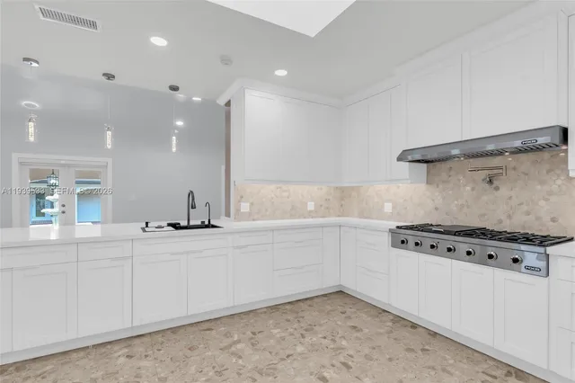 a large white kitchen with kitchen island a stove a sink a refrigerator and white cabinets