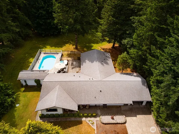 an aerial view of a house with swimming pool and trees all around