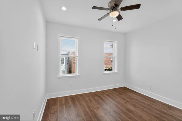 an empty room with wooden floor ceiling fan and windows