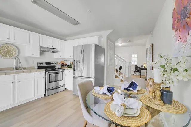 a kitchen with stainless steel appliances a refrigerator a sink a stove a dining table and chairs with wooden floor