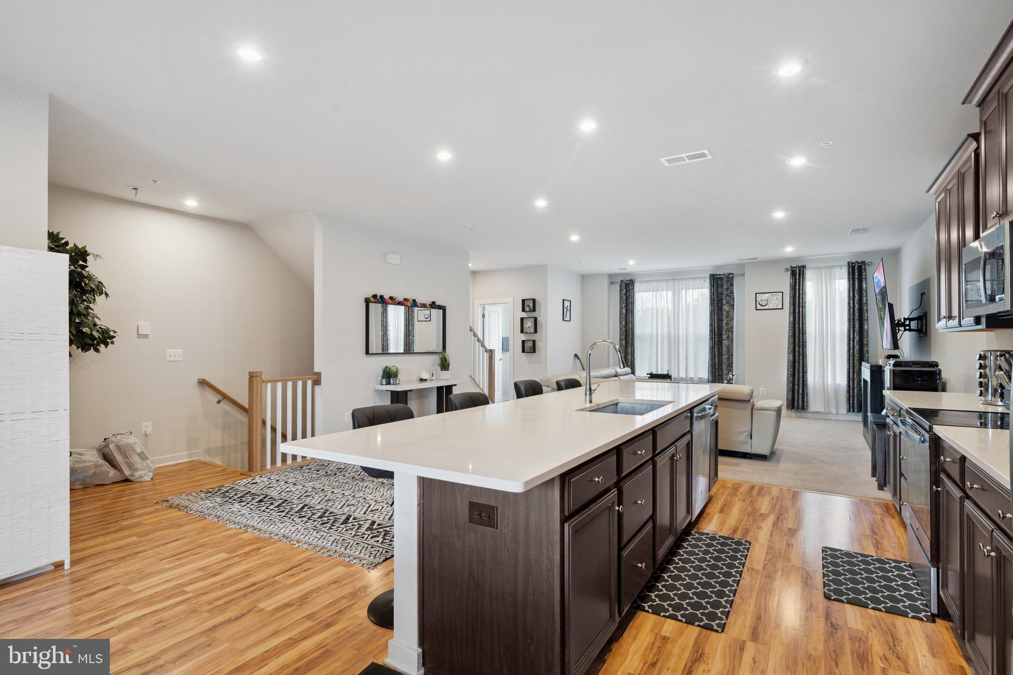 13506 Innovation Station Loop, Unit 2B Herndon, VA 20171 - Photo 5 of 32 a large kitchen with kitchen island a stove a sink dishwasher and a dining table with wooden floor