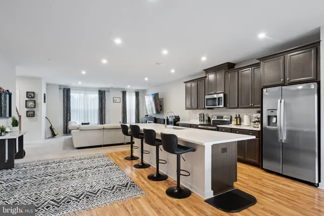 a large kitchen with stainless steel appliances kitchen island granite countertop a refrigerator a stove a sink a dining table and chairs with wooden floor