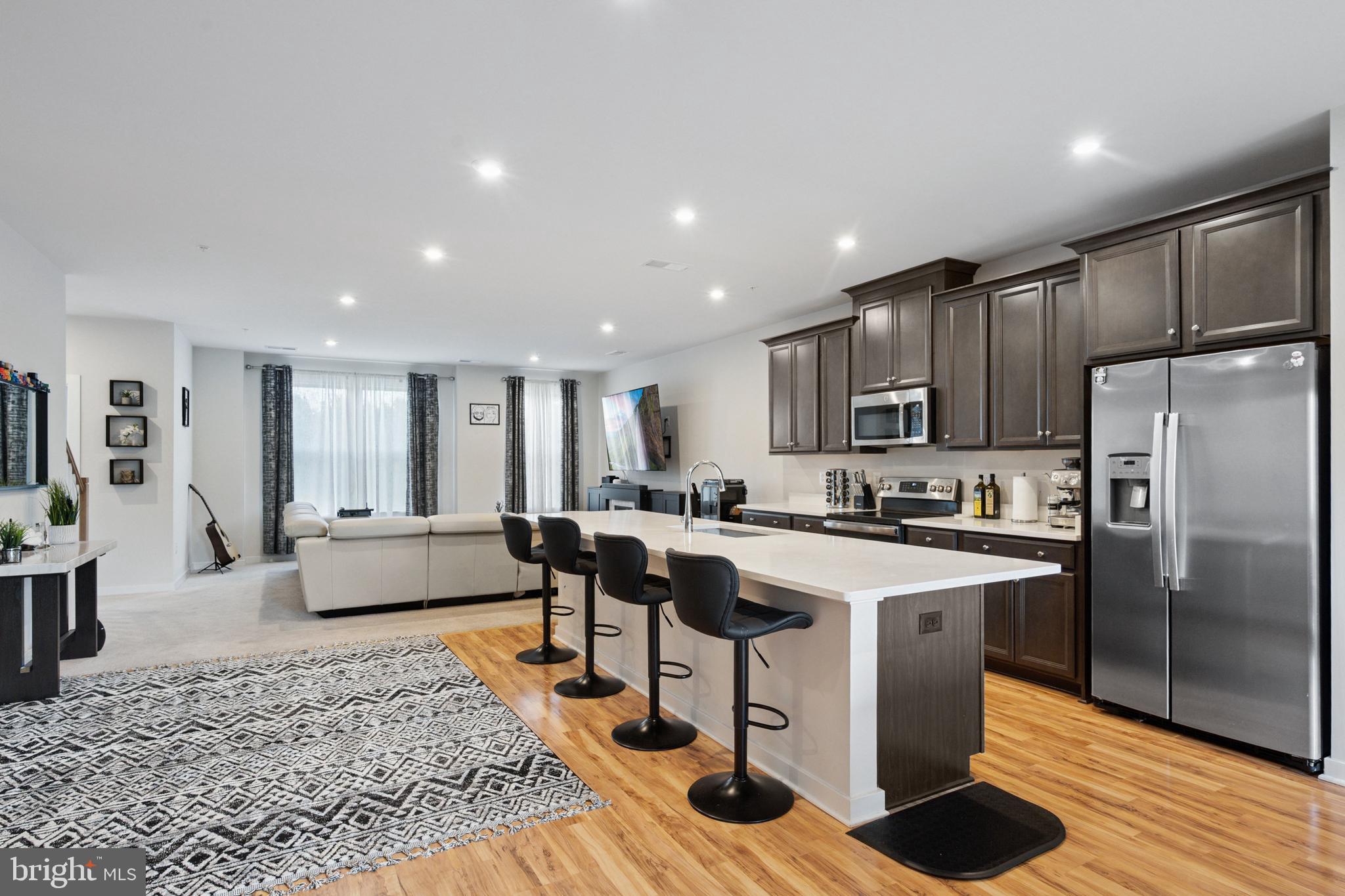 13506 Innovation Station Loop, Unit 2B Herndon, VA 20171 - Photo 8 of 32 a large kitchen with stainless steel appliances kitchen island granite countertop a refrigerator a stove a sink a dining table and chairs with wooden floor