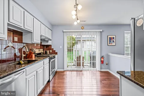 a kitchen with stainless steel appliances granite countertop a stove top oven a sink dishwasher a dining table and chairs with wooden floor