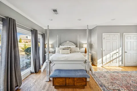 a bedroom with a bed window and walk in closet with wooden floor