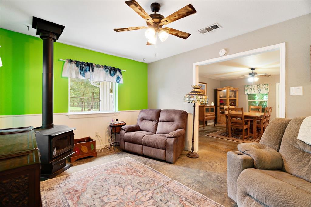 821 County Road Paris, TX 75462 - Photo 27 of 40 Living area featuring a freestanding wood-burning stove, ceiling fan with light fixture, and a window with exterior views