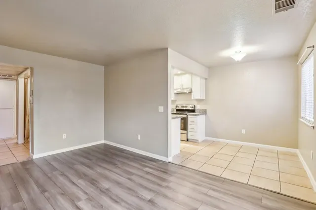 a view of an empty room with kitchen and window