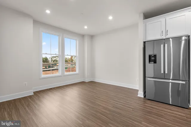 a view of an empty room with wooden floor fridge and a window