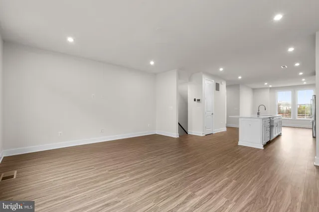 a view of an empty room with wooden floor and a kitchen