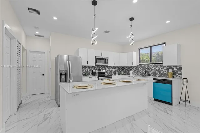 a large kitchen with stainless steel appliances kitchen island granite countertop a refrigerator a stove a sink dishwasher and a oven with white cabinets