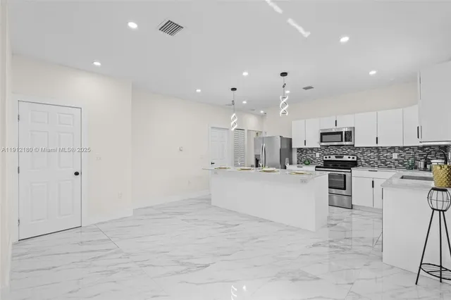 a large white kitchen with white cabinets stainless steel appliances and a chandelier